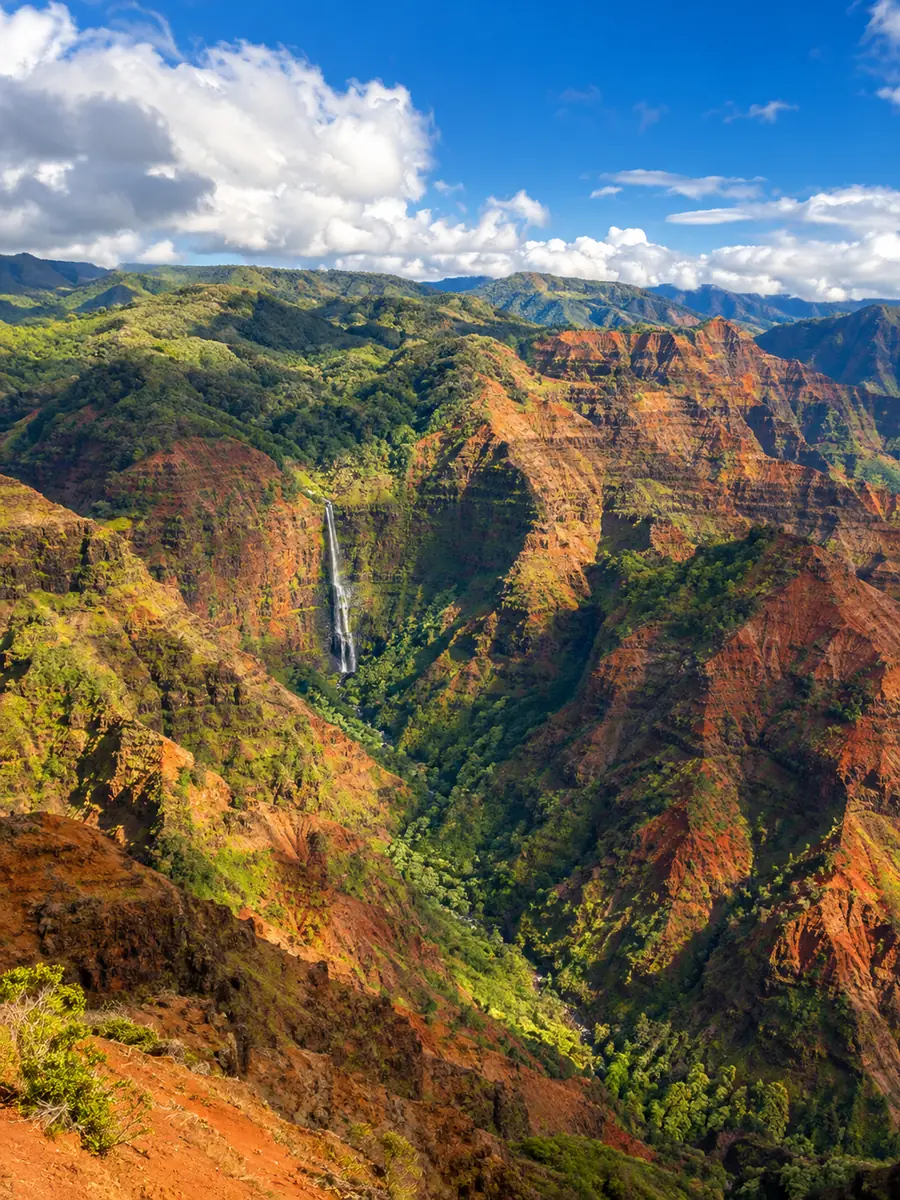 Crêtes rouges et vertes de Waimea Canyon avec une fine cascade, vues du ciel