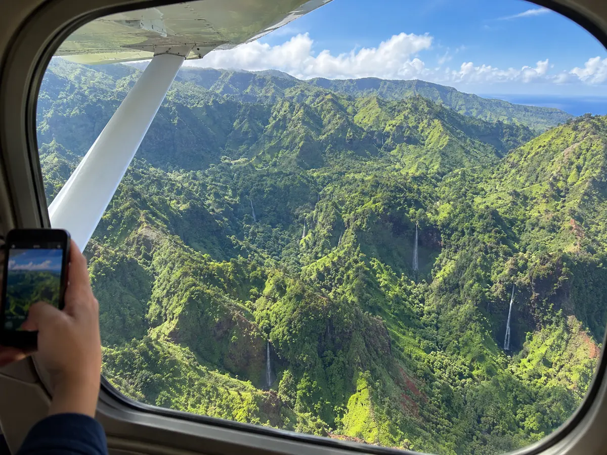Vue à travers le hublot bombé d'un petit avion sur des vallées verdoyantes et des cascades